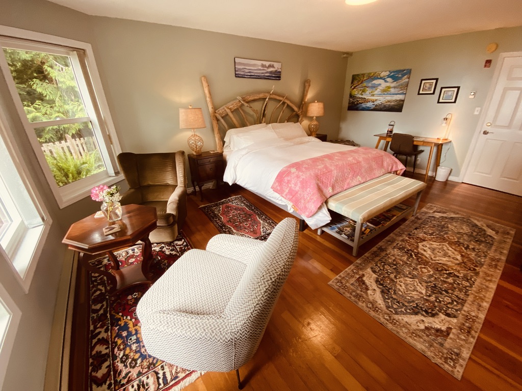 The Sea Glass Suite at Ocean Wilderness Inn featuring bright wraparound windows, a luxury king bed, and a cozy reading chair in Shirley, BC.
