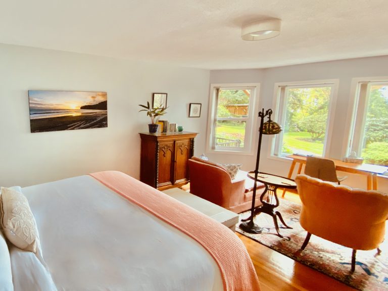 The Driftwood Suite at Ocean Wilderness Inn featuring a custom artisan headboard, luxury king bedding, and bright garden views in Shirley, BC.