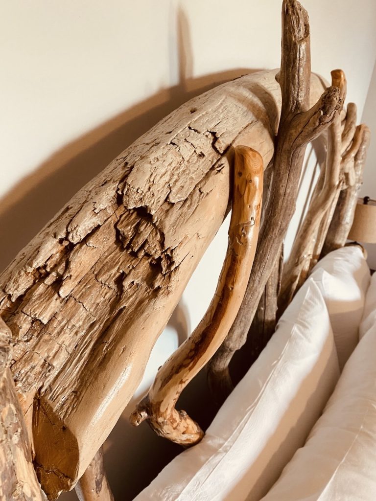 Hand-carved driftwood headboard in a bright, boutique guest suite at Ocean Wilderness Inn, showcasing artisan West Coast interior design in Shirley, BC.