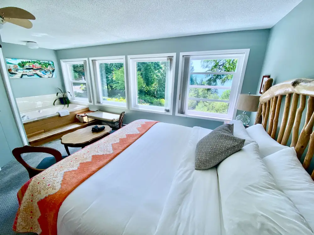 Bright oceanfront Salish Sea Suite at Ocean Wilderness Inn featuring a king bed, large soaker tub, rustic wood headboard, and panoramic water views.