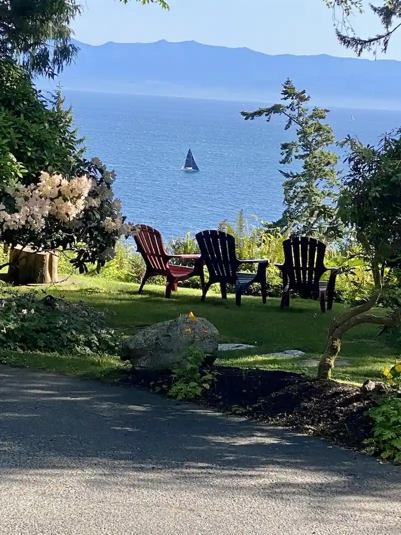 Two red Adirondack chairs on a lush green lawn overlooking the Salish Sea at Ocean Wilderness Inn, Shirley BC.