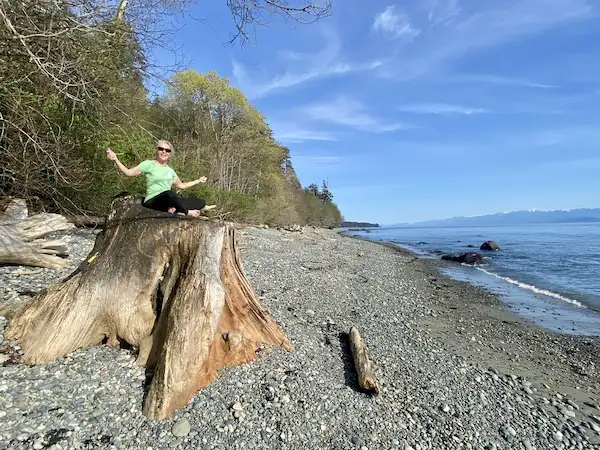 Woman practicing yoga on a driftwood stump at Ocean Wilderness Inn’s private beach access in Shirley, BC, overlooking the Olympic Mountains.