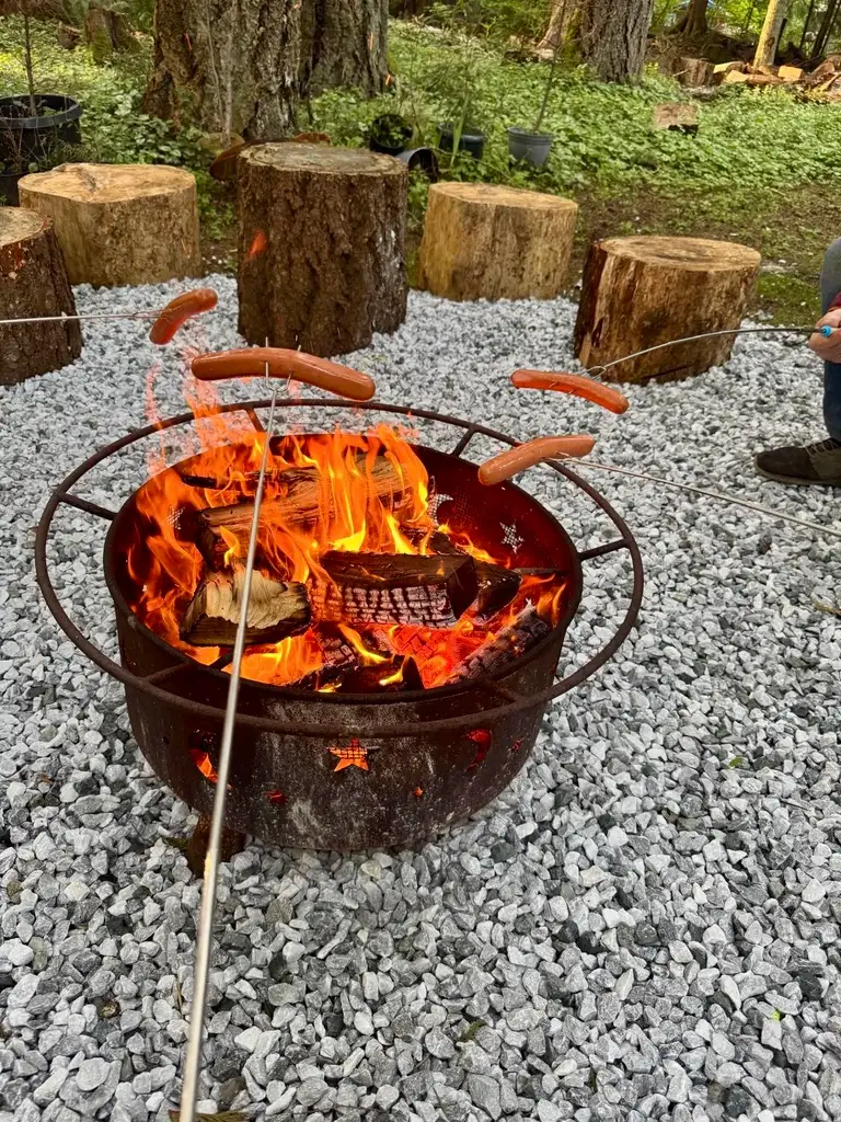 uests roasting hot dogs over the custom fire pit on a gravel terrace surrounded by rustic log seating at Ocean Wilderness Inn.
