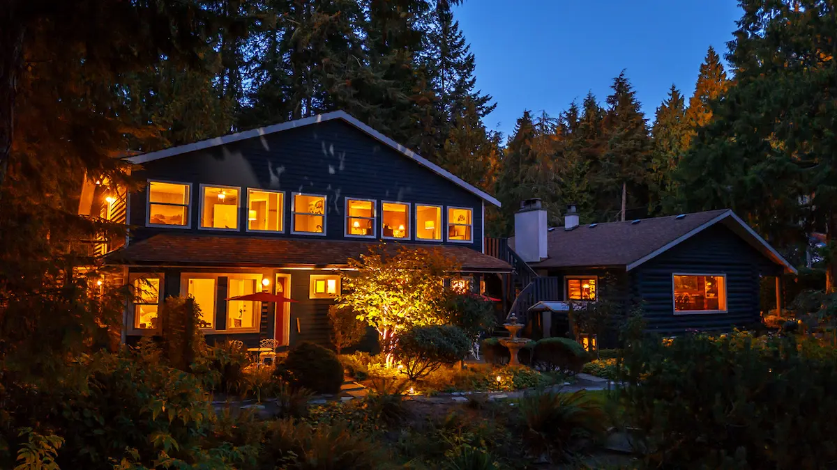 Exterior view of Ocean Wilderness Inn and the Historic Log Cabin glowing warmly at twilight in Shirley BC near Sooke