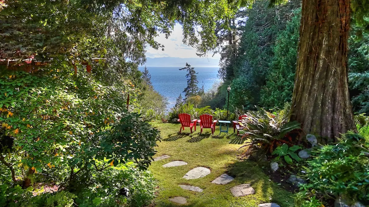 Oceanfront garden lawn with red Adirondack chairs overlooking the Salish Sea at Ocean Wilderness Inn near Sooke, Shirley BC